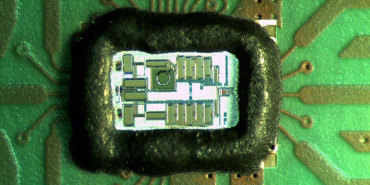 A close-up of a small electronic chip, possibly showing complex circuitry, presented on a larger circuit board.